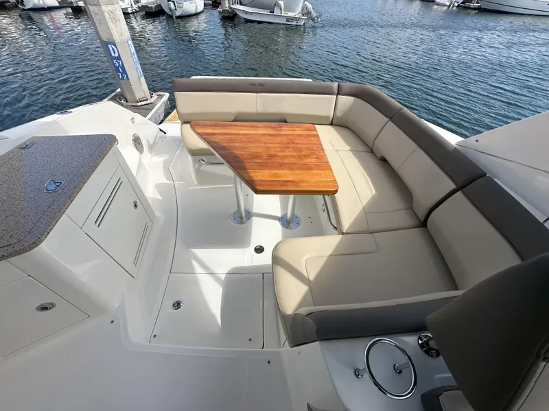 Slide: The Image of 2015 Sea Ray 350 Sundancer boat interior with seating and wooden table by the water. - 16