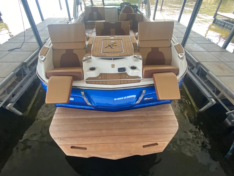 Slide: The Image of 2022 MasterCraft X26 boat with blue hull, docked, featuring luxurious seating and swim platform. - 14