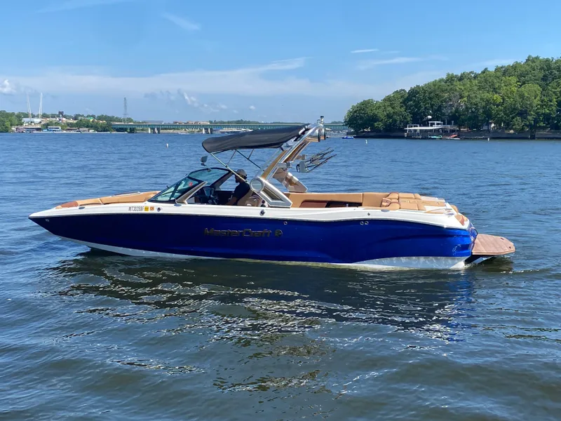 Slide: The Image of 2022 MasterCraft X26 boat on a lake with lush green shoreline. - 2