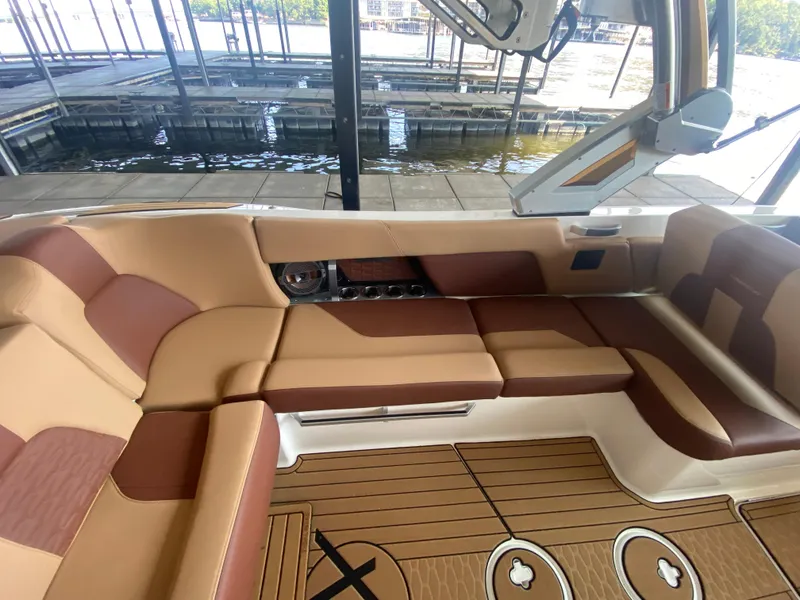 Slide: The Image of 2022 MasterCraft X26 boat interior with tan and brown seating, docked by the water. - 22