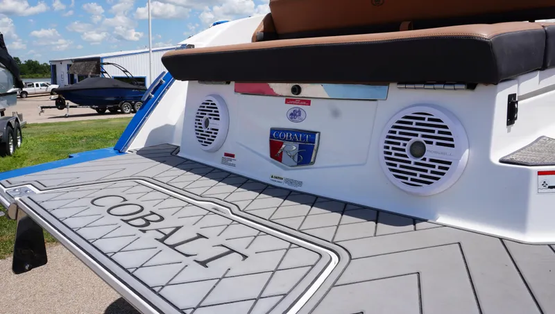 Slide: The Image of 2022 Cobalt R6 boat rear deck with speakers and logo, parked outdoors. - 13