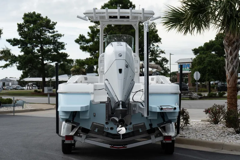Slide: The Image of 2026 Caymas 24 HB boat, rear view, parked outdoors with trees and buildings in background. - 6