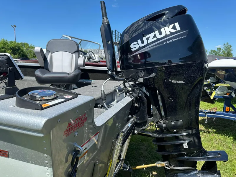Slide: The Image of 2023 Alumacraft Competitor 185 Tiller with Suzuki outboard motor, parked on grass. - 21
