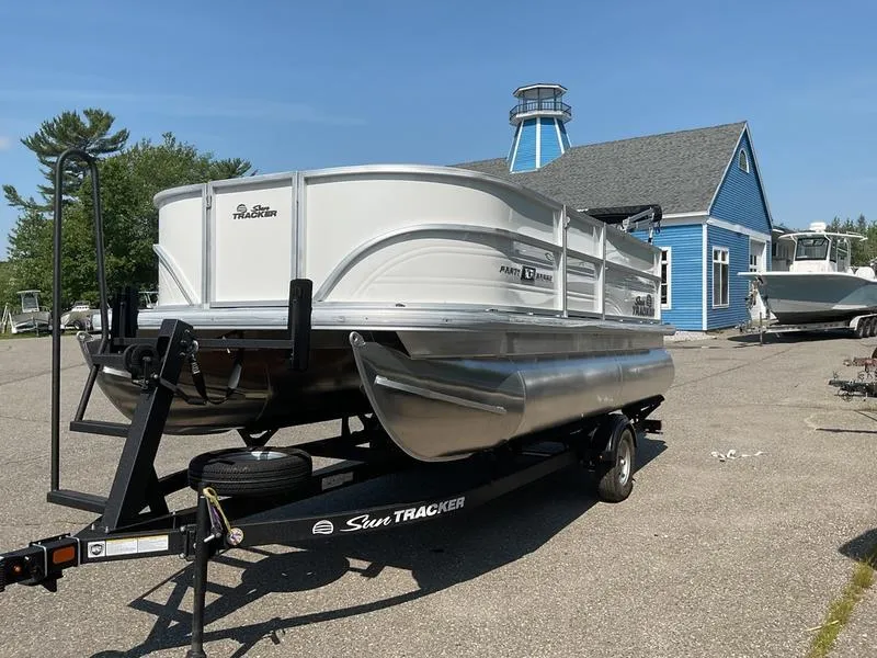 Slide: The Image of 2026 Sun Tracker PB 16 DLX pontoon boat on trailer, parked near blue building. - 9