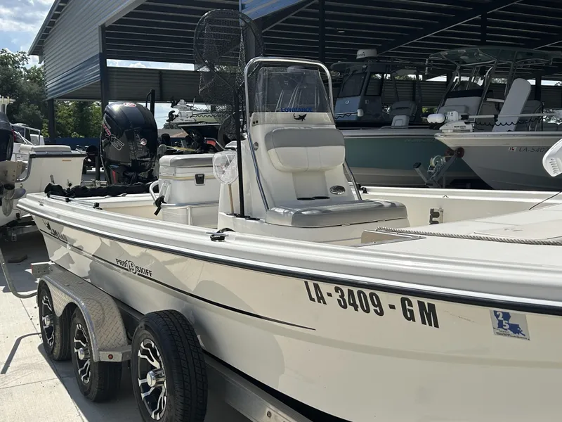 Slide: The Image of 2021 Mako Pro Skiff 19 CC boat on trailer, parked under a metal canopy. - 2