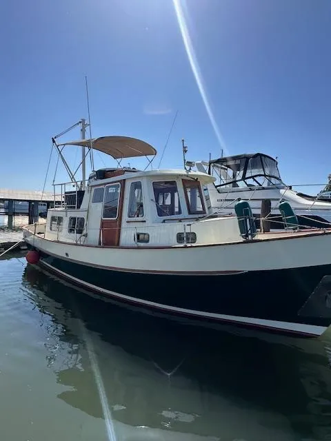 Slide: The Image of 1985 Ankertrawler Trawler interior with wooden table, cushioned seating, and windows overlooking the water. - 2