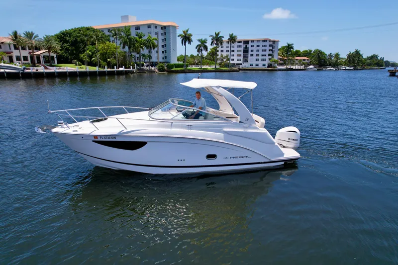 Slide: The Image of 2021 Regal 26 XO boat cruising on a sunny day in a scenic waterfront area. - 2
