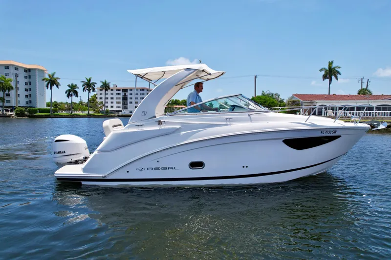 Slide: The Image of 2021 Regal 26 XO boat cruising on a sunny day, with modern buildings in the background. - 5