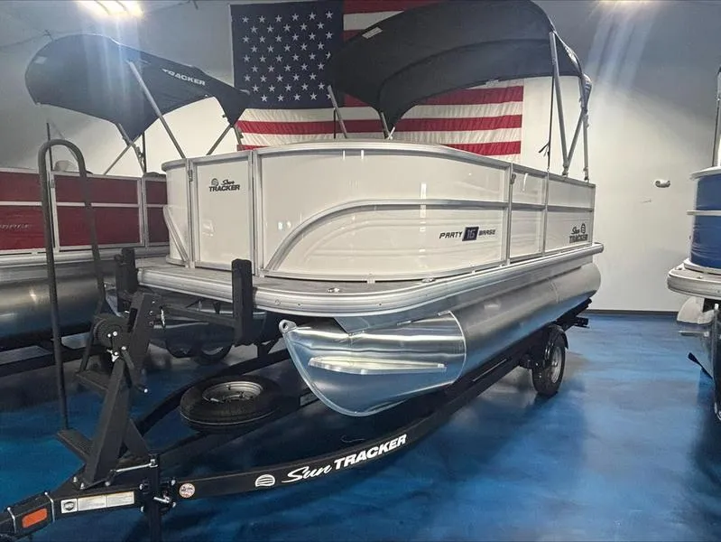 Slide: The Image of 2026 Sun Tracker PB 16 DLX pontoon boat on trailer, displayed indoors with American flag backdrop. - 9