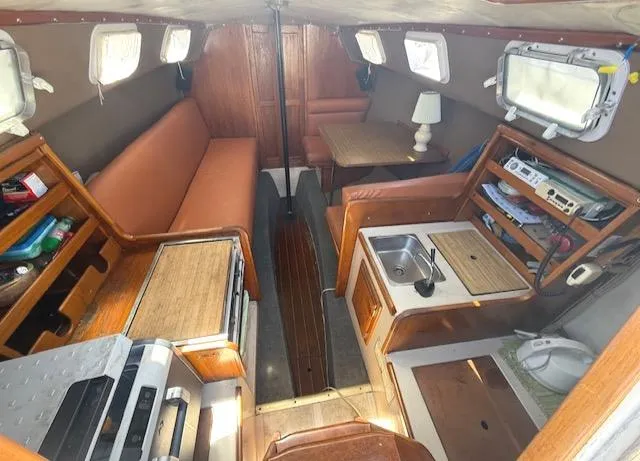 Slide: The Image of Interior of a 1979 Lancer Sloop sailboat with cozy seating, kitchenette, and wooden accents. - 14