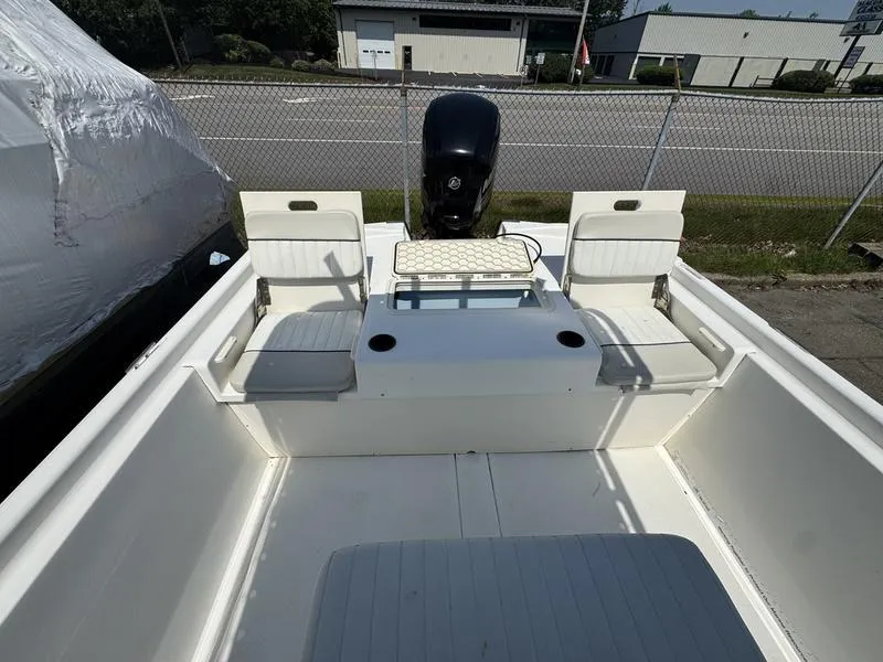 Slide: The Image of 2017 Mako 21 Pro Skiff CC boat interior with seating and motor, parked near a fence. - 4