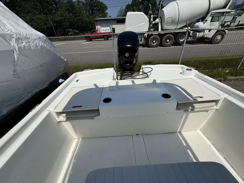 Slide: The Image of 2017 Mako 21 Pro Skiff CC boat interior with motor, parked near a fence. - 5