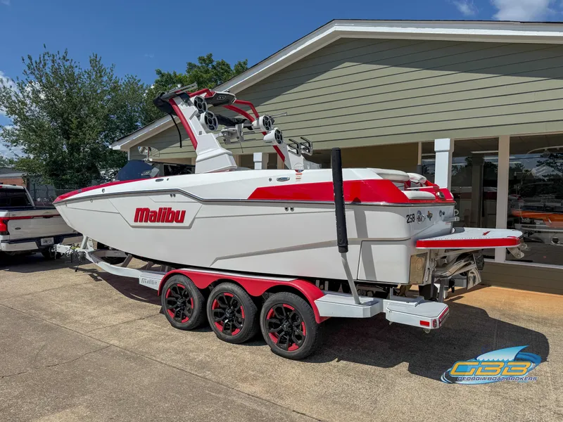 Slide: The Image of 2021 Malibu M240 boat on a red trailer, parked outside a building. - 11