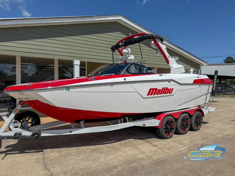 Slide: The Image of 2021 Malibu M240 boat with red and white design on a trailer, parked outdoors. - 12
