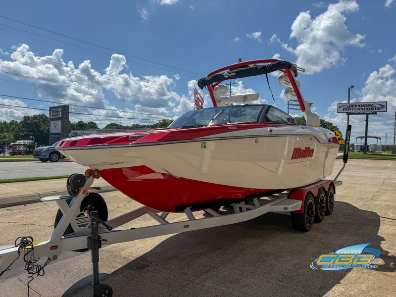 Slide: The Image of 2021 Malibu M240 boat on trailer, parked outdoors under a blue sky. - 14