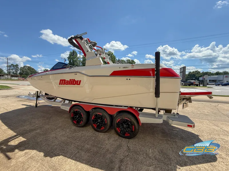 Slide: The Image of 2021 Malibu M240 boat on trailer, red and white design, parked outdoors under blue sky. - 15