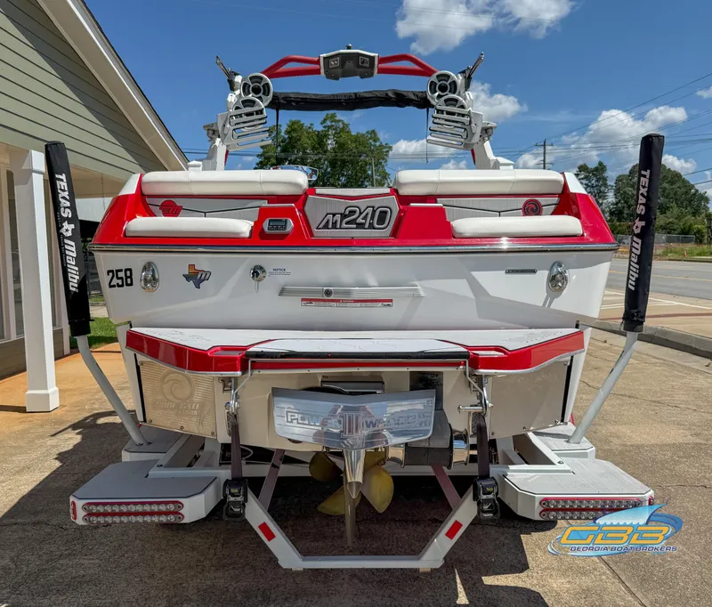Slide: The Image of 2021 Malibu M240 boat, red and white, parked outdoors, showcasing rear design and features. - 18