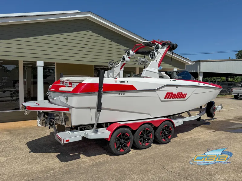 Slide: The Image of 2021 Malibu M240 boat on trailer, white and red design, parked outside a building. - 20