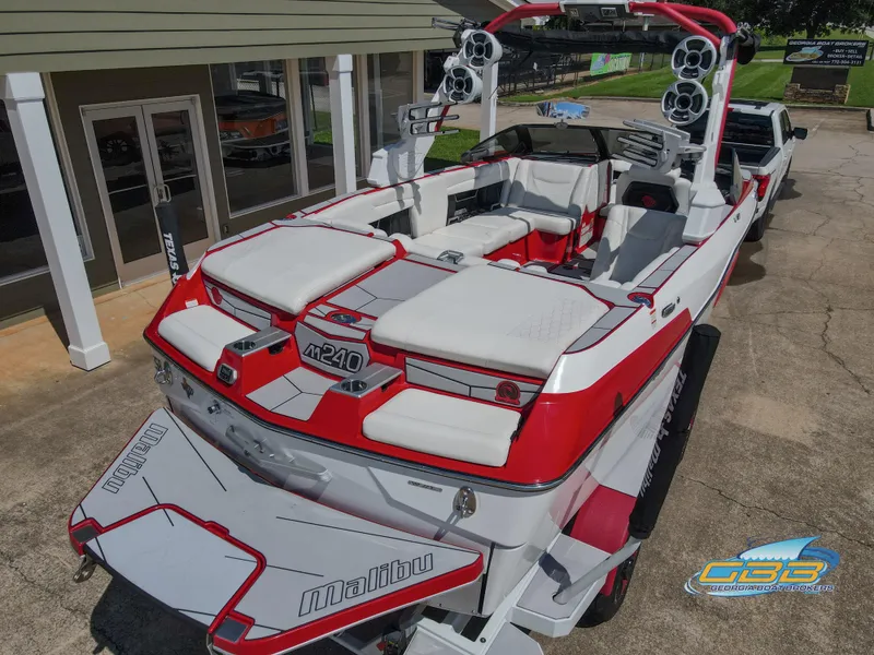Slide: The Image of 2021 Malibu M240 boat with red and white design, parked outdoors. - 7