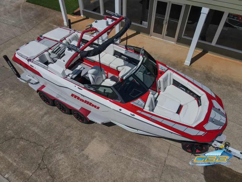 Slide: The Image of 2021 Malibu M240 boat with red and white design, parked on concrete near a building. - 9