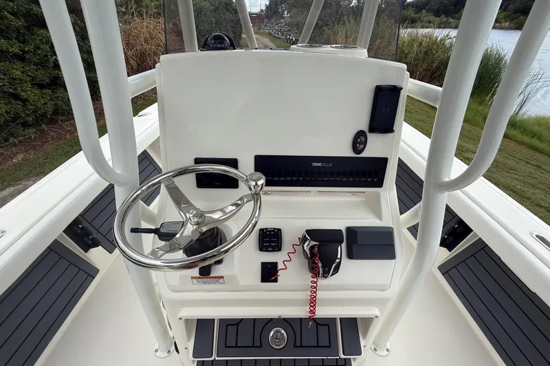 Slide: The Image of 2025 Pathfinder 2400 TRS boat console with steering wheel and controls, near waterway. - 16