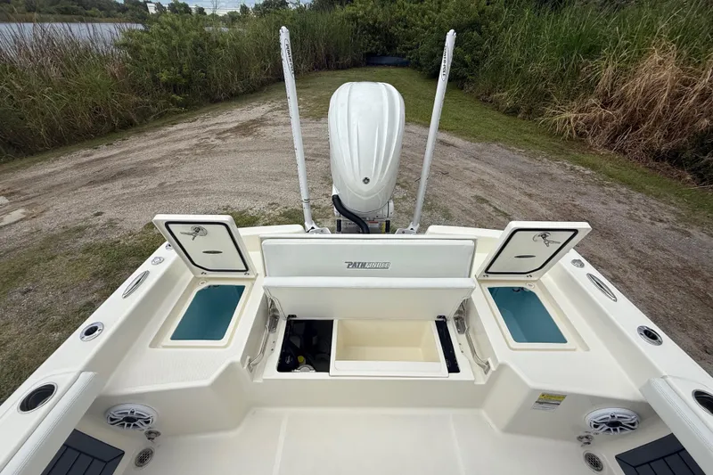 Slide: The Image of 2025 Pathfinder 2400 TRS boat with open storage compartments and motor, near a grassy shoreline. - 26