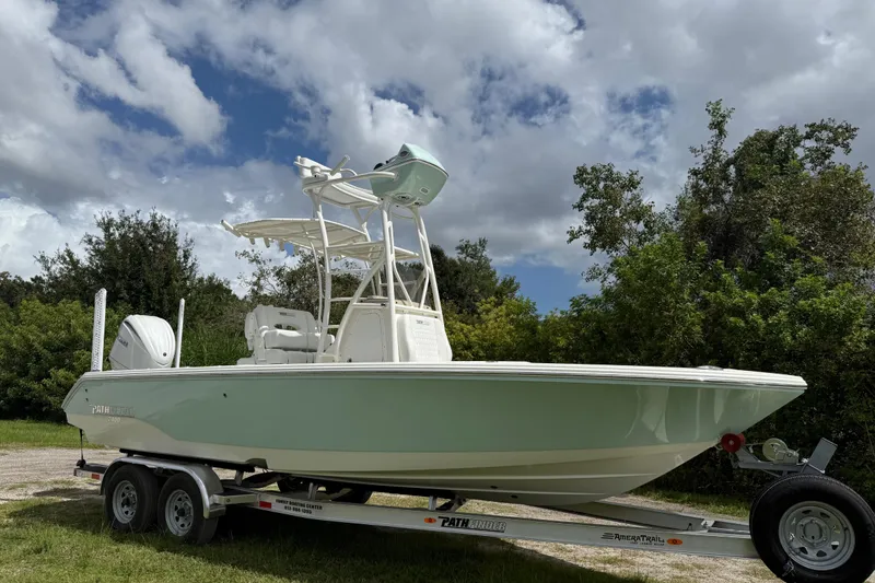 The Image of 2025 Pathfinder 2400 Open boat on trailer, set against a cloudy sky and greenery. - 0