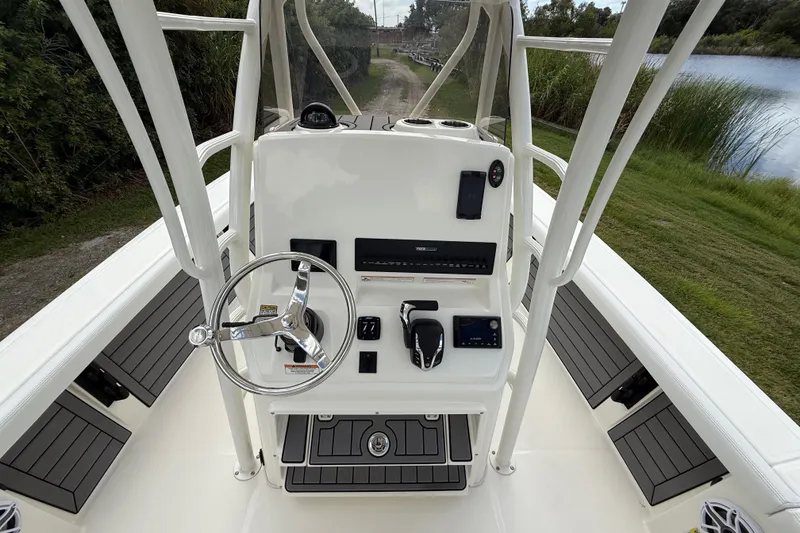 Slide: The Image of 2025 Pathfinder 2400 Open boat console with steering wheel and controls, near water and greenery. - 16