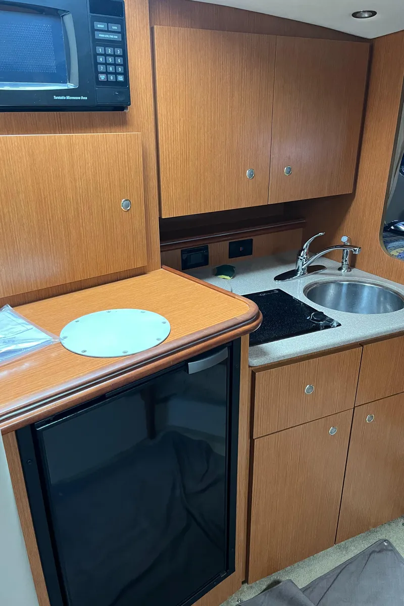 Slide: The Image of 2004 Cruisers Yachts 320 Express kitchen with wood cabinets, sink, microwave, and mini-fridge. - 24