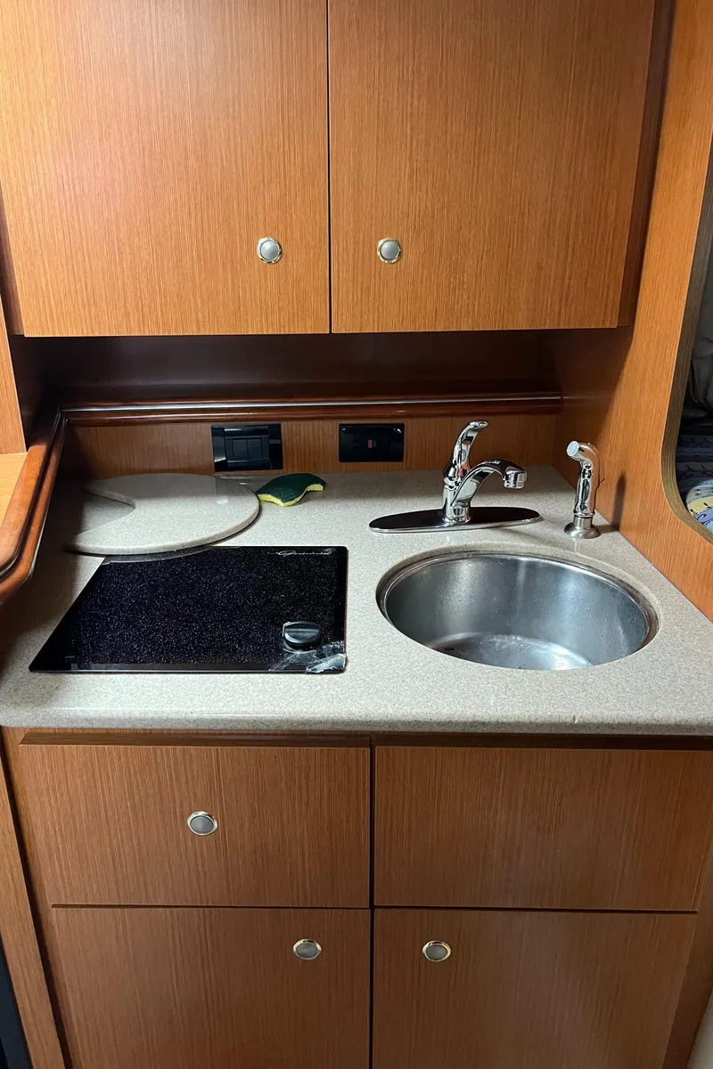 Slide: The Image of 2004 Cruisers Yachts 320 Express kitchen with sink, stove, and wooden cabinets. - 26