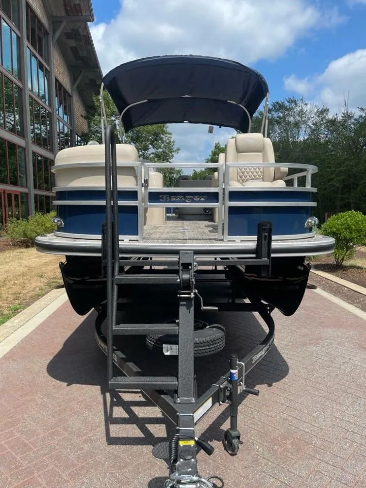 Slide: The Image of 2025 Ranger Reata 220FC pontoon boat on trailer, parked outdoors under blue sky. - 2