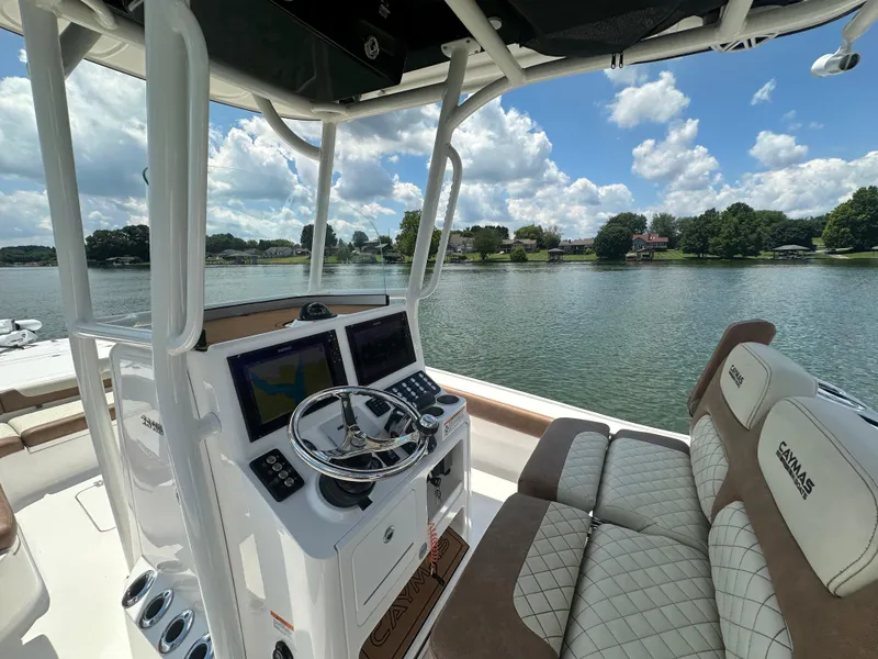 Slide: The Image of 2023 Caymas 26 HB boat interior with steering console, dual screens, and cushioned seating on a lake. - 11
