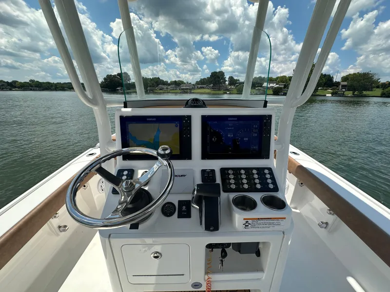Slide: The Image of 2023 Caymas 26 HB boat dashboard with steering wheel and navigation screens on a sunny day. - 23