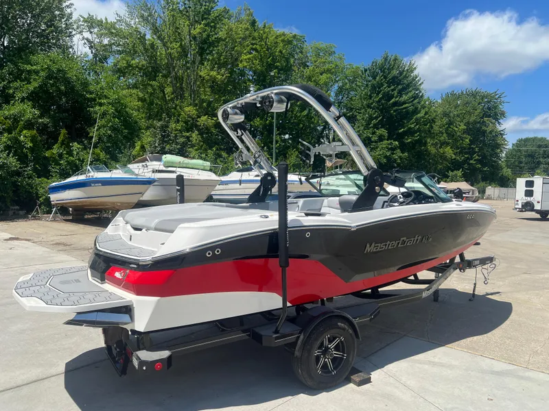 Slide: The Image of 2020 MasterCraft NXT20 boat on trailer, parked outdoors with trees in background. - 4