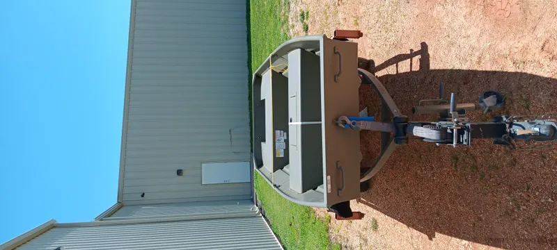 Slide: The Image of 2026 Tracker 1542 JON boat on trailer, parked beside a metal building. - 6