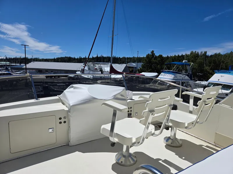 Slide: The Image of 1990 Tollycraft Sport Sedan boat deck with chairs, marina background, clear sky. - 22