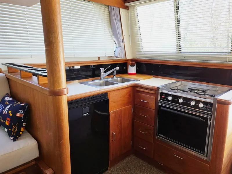 Slide: The Image of 1990 Tollycraft Sport Sedan kitchen with wood cabinetry, stove, sink, and blinds. - 42