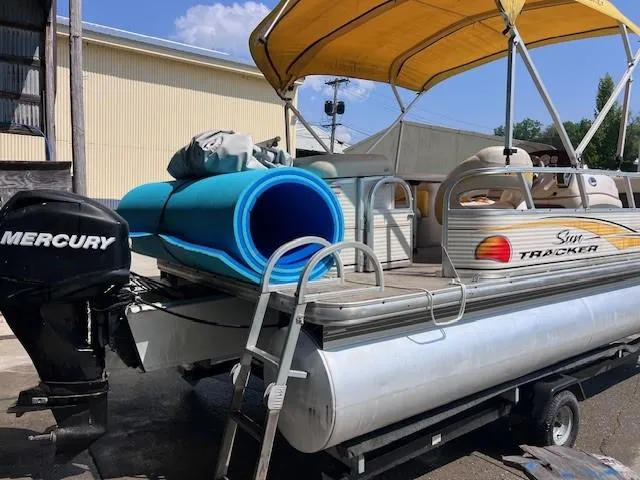 Slide: The Image of 2010 Sun Tracker PARTY BARGE 21 with Mercury engine and blue mats, parked outdoors. - 2