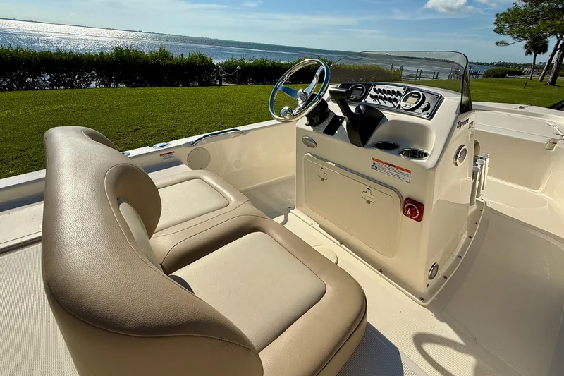 Slide: The Image of 2026 Scout 177 Sport boat interior with steering console, beige seating, and scenic waterfront view. - 13