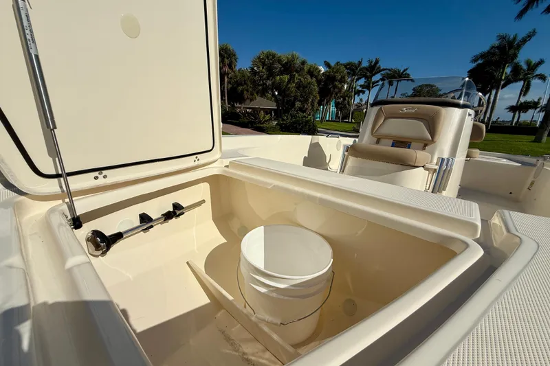 Slide: The Image of 2026 Scout 177 Sport boat interior with storage compartment and seating, surrounded by palm trees. - 20