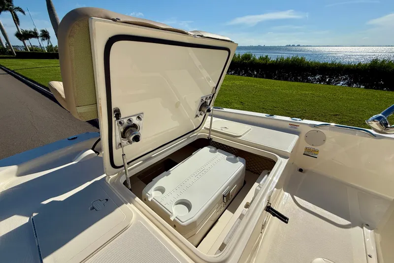 Slide: The Image of 2026 Scout 177 Sport boat with open storage compartment and cooler, near scenic waterfront. - 7