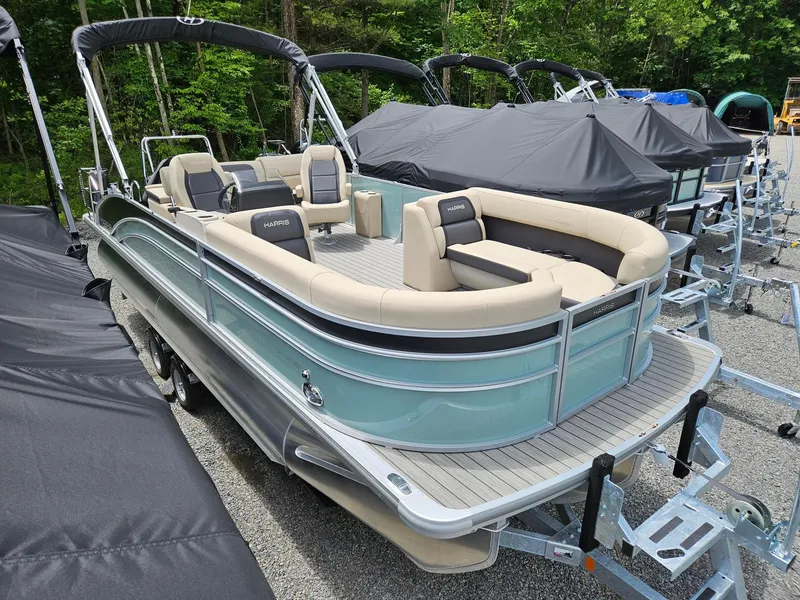 Slide: The Image of 2024 Harris Cruiser 230 pontoon boat with beige seating, parked on a trailer. - 2