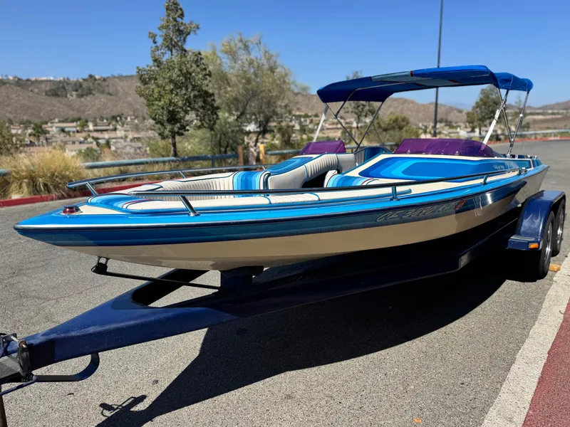 Slide: The Image of 1987 Bahner 19 BR speedboat with blue and white design on a trailer, parked outdoors. - 3
