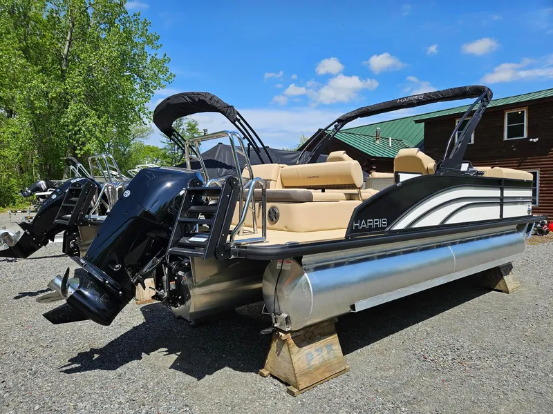 Slide: The Image of 2025 Harris Sunliner 230 pontoon boat with outboard motor, parked outdoors on a sunny day. - 2