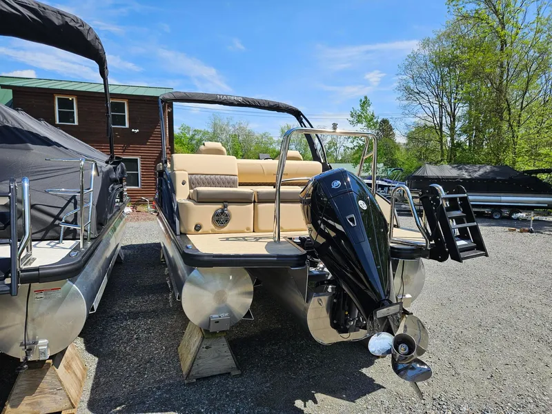Slide: The Image of 2025 Harris Sunliner 230 pontoon boat with outboard motor, parked outdoors on a sunny day. - 3