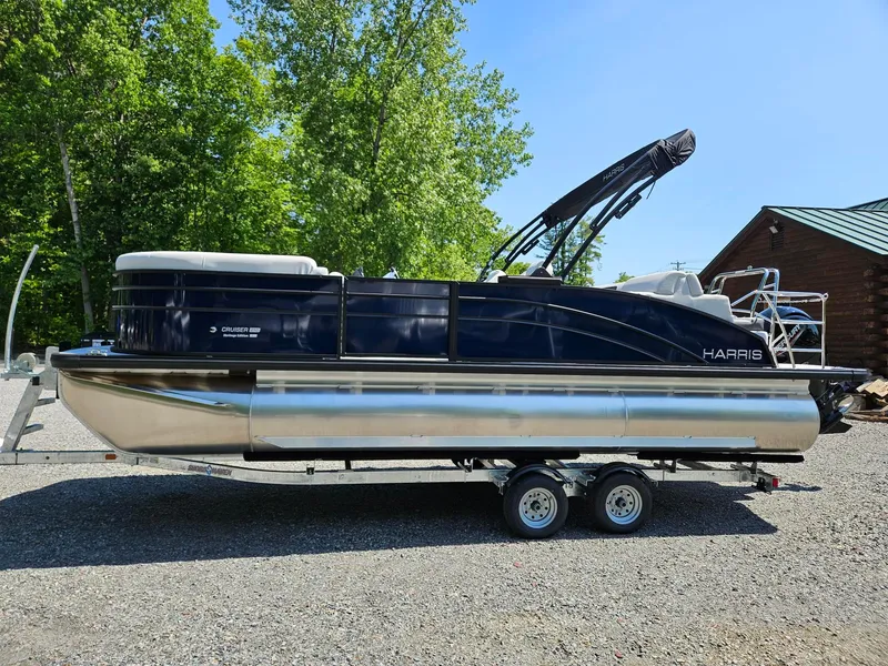 Slide: The Image of 2025 Harris Cruiser 210 pontoon boat on trailer, surrounded by trees and clear sky. - 2