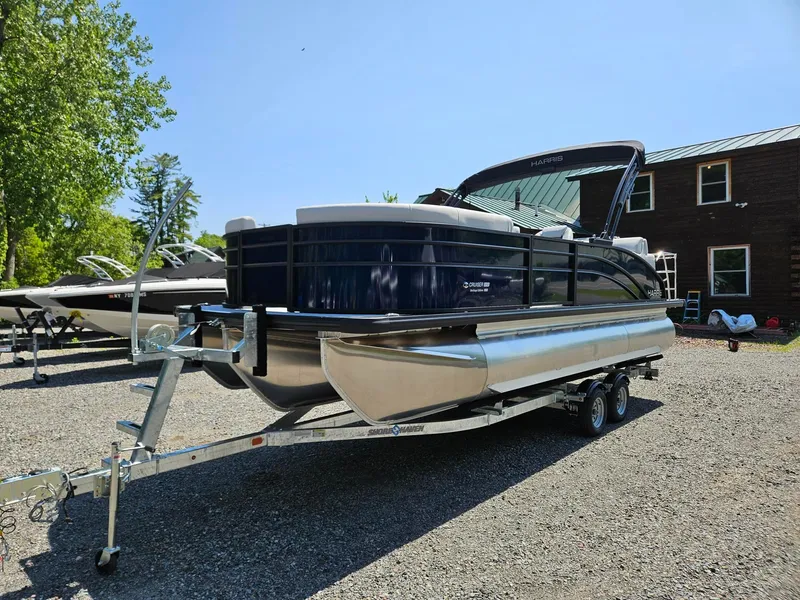 Slide: The Image of 2025 Harris Cruiser 210 pontoon boat on trailer, parked outdoors under clear blue sky. - 3