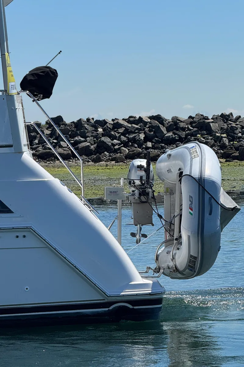 Slide: The Image of 1997 Carver 405 Aft Cabin Motoryacht with dinghy, docked near rocky shoreline. - 3