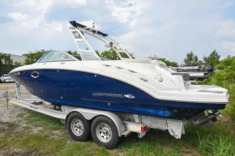 Slide: The Image of 2018 Chaparral 264 Sunesta boat on trailer, blue and white design, parked outdoors. - 4