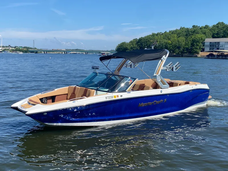 The Image of 2022 MasterCraft X26 boat on a lake with blue water and green trees. - 0